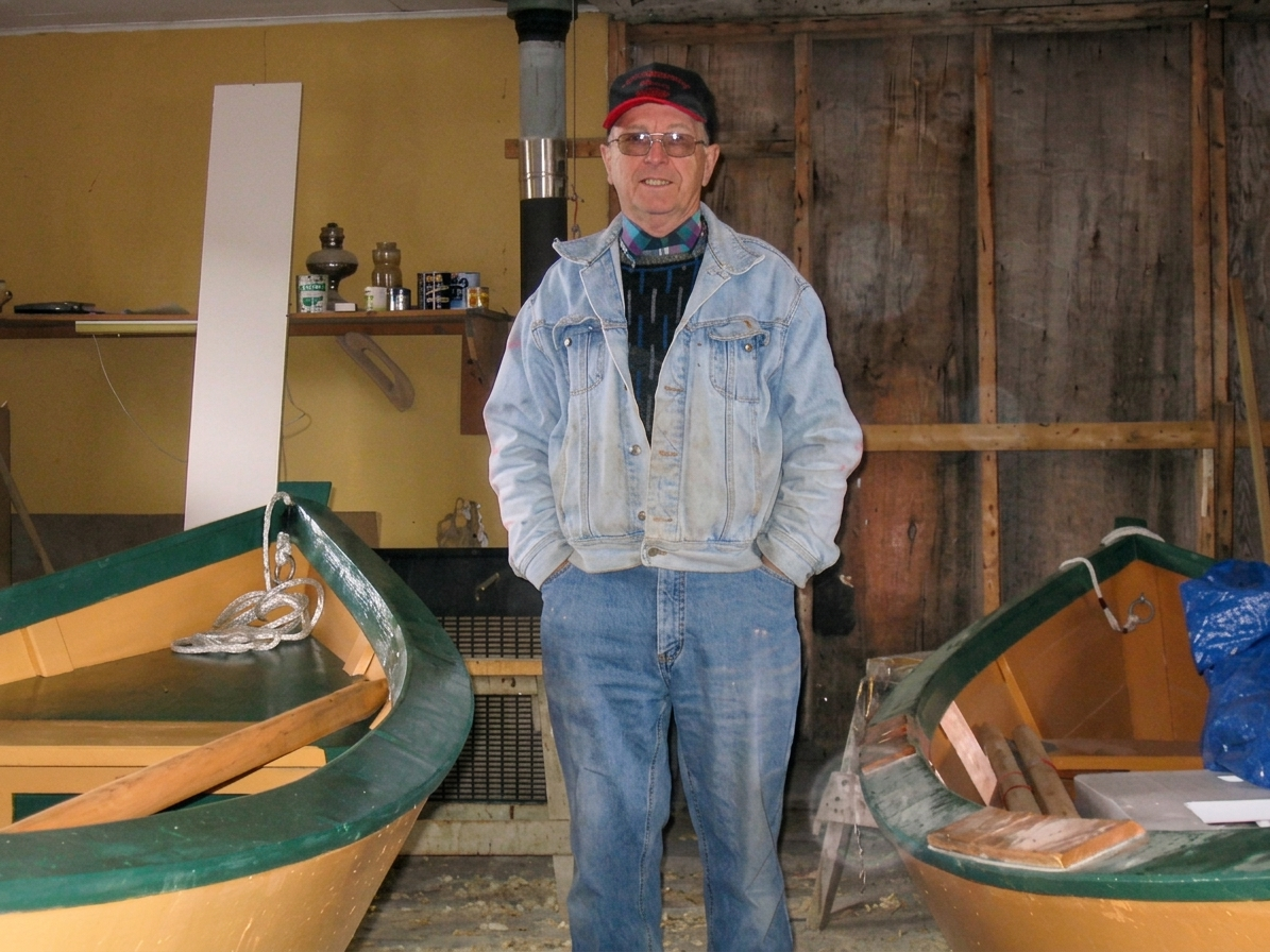 Wilbert Weir resting his hand on the bow of a dory he's building